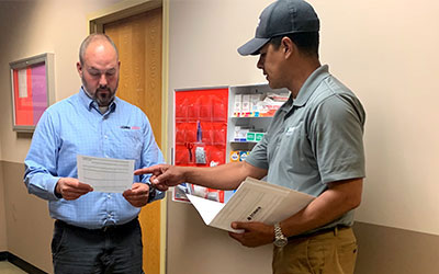 A Lechner First Aid Service Representative and a Safety Manager discussing a safety brochure in front of a first aid cabinet.