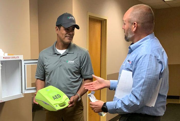 A Lechner First Aid Service Representative standing in front of a Zoll AED Plus unit.