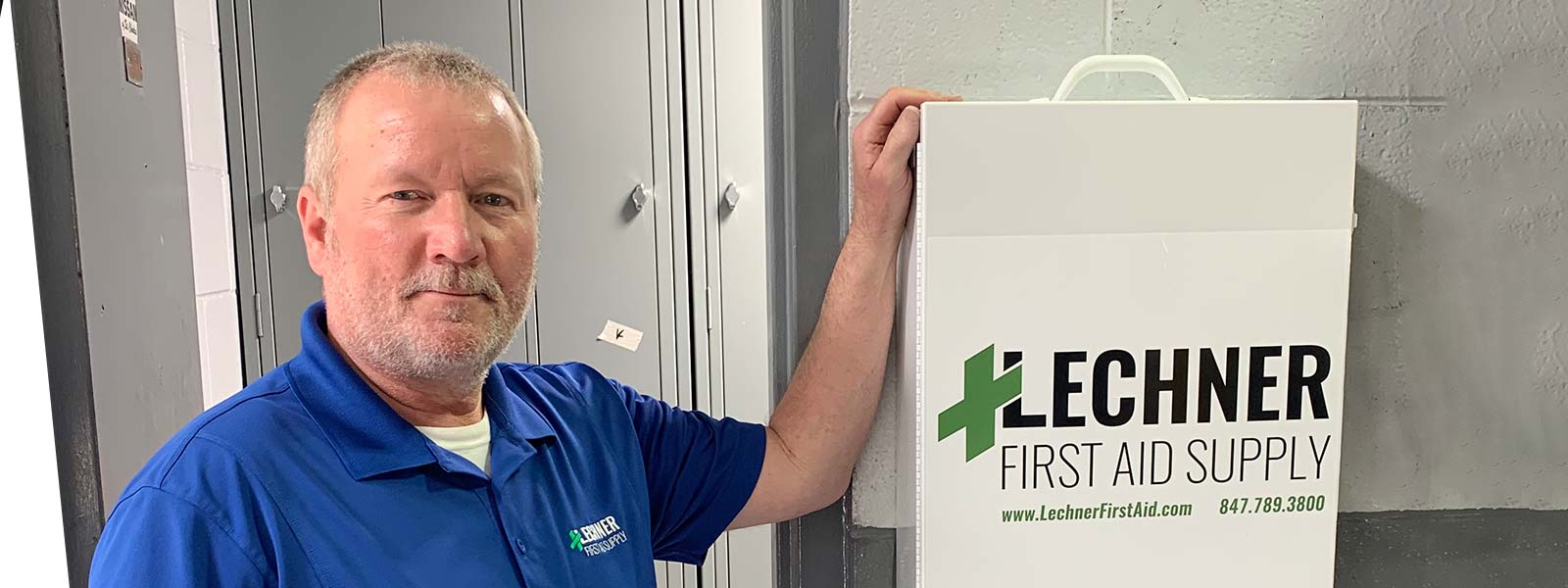 A Lechner First Aid Service employee stands by a Lechner First Aid cabinet/ First Aid box. 