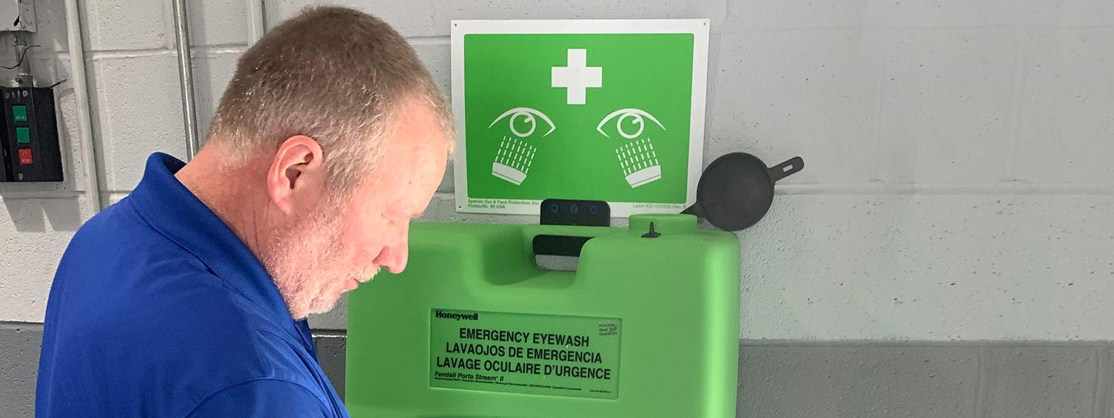 Lechner First Aid Service employee standing in front of a green eye washing station.